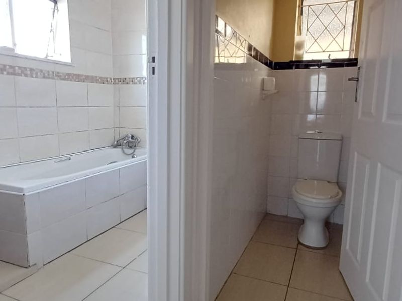 A functional bathroom featuring a built-in bathtub and a separate toilet area with tiled walls and floors.