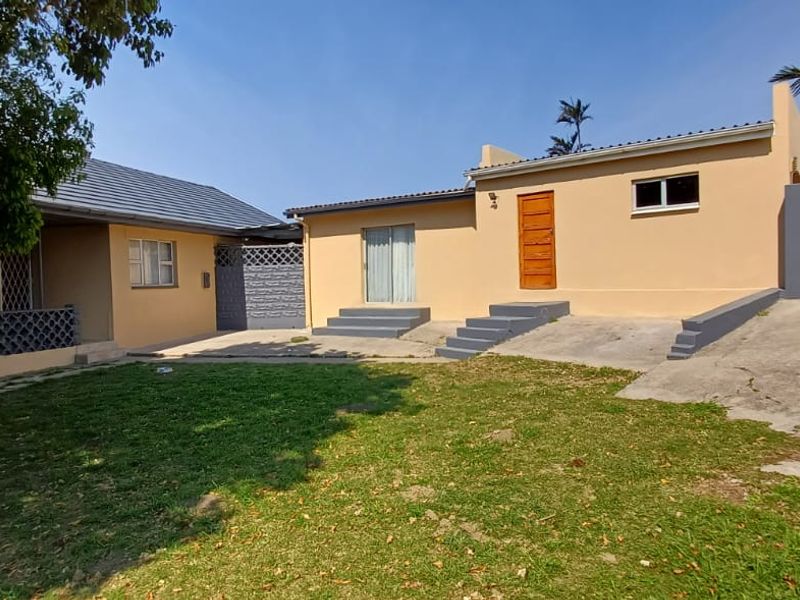 Rear view of the property featuring a concrete driveway, lawn area, and access to the main dwelling via sliding glass and timber doors.