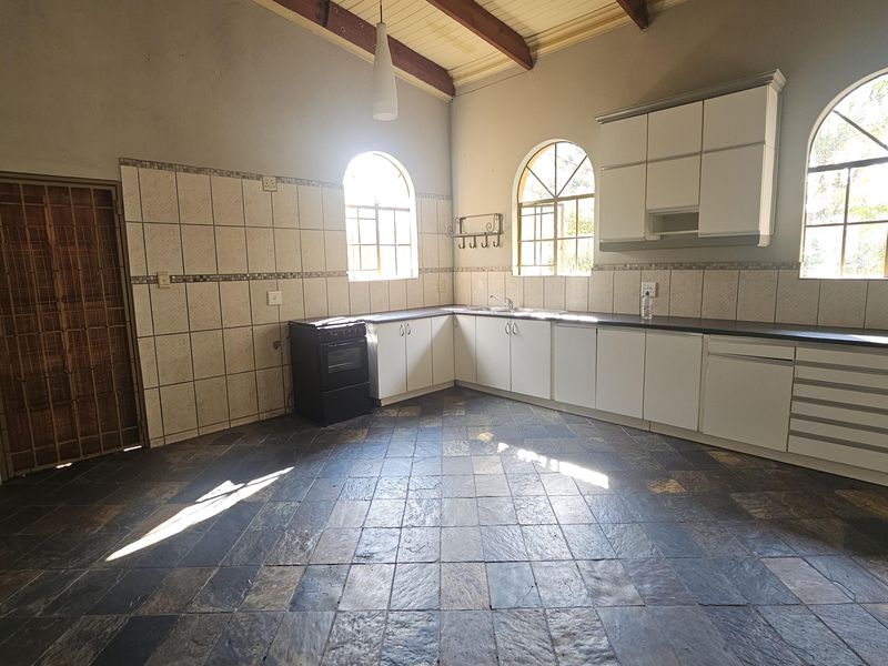 Spacious kitchen featuring white cabinetry, dark countertops, tiled flooring, and exposed timber beams, illuminated by natural light through arched windows.