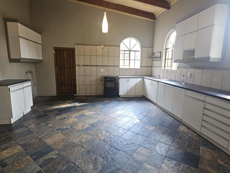 Spacious kitchen featuring stone tile flooring, ample built-in cabinetry, arched windows, and exposed timber ceiling beams, offering a functional layout ready for modernization.