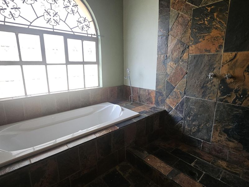 Spacious bathroom featuring a built-in bathtub, a walk-in shower with slate tile finishes, and an arched window with decorative wrought iron detailing.