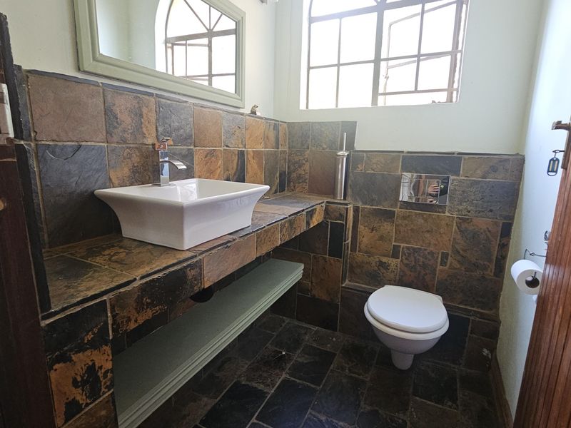 A compact bathroom featuring slate tile finishes, a modern vessel sink on a built-in vanity, and a wall-mounted toilet.