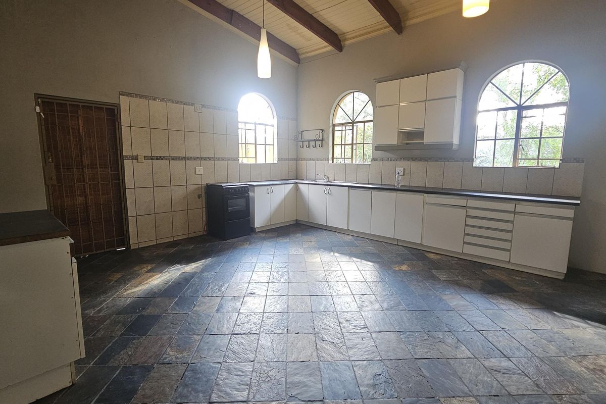 Spacious kitchen featuring slate flooring, exposed timber ceiling beams, arched windows, and ample built-in cabinetry with a functional layout.