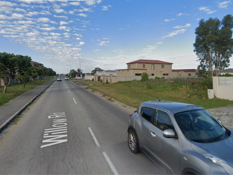 A street view of Willow Road showing the surrounding residential neighborhood, paved road, and boundary walls of adjacent properties.