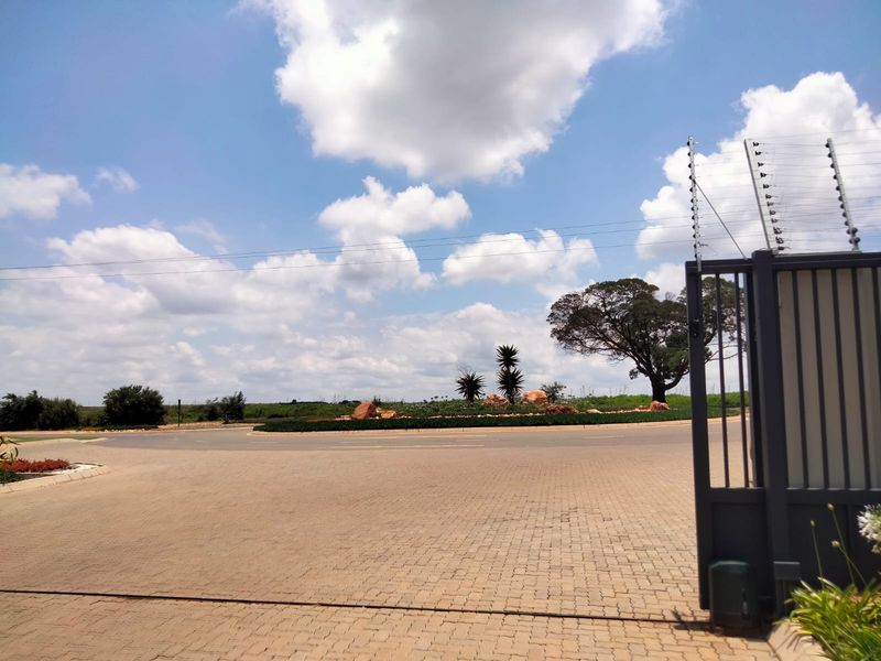 View of the retirement village entrance featuring a paved driveway, secure electric gate, and electric fencing surrounding the perimeter.