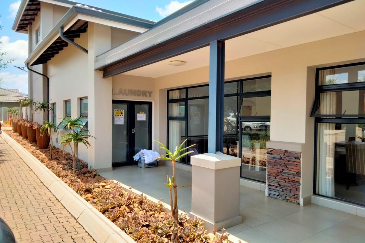 A well-maintained exterior view of a retirement village facility featuring a covered patio, stone cladding accents, and paved walkways with landscaped garden beds.