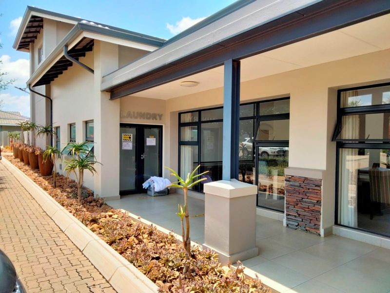 A well-maintained exterior view of a retirement village facility featuring a covered patio, stone cladding accents, and paved walkways with landscaped garden beds.
