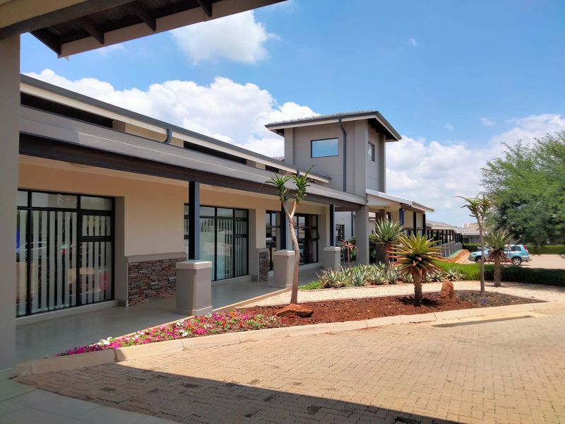 A well-maintained retirement village exterior featuring a covered walkway, stone-clad pillars, paved driveway, and landscaped garden beds.