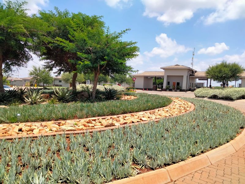 A well-maintained entrance to the retirement village featuring landscaped gardens, paved driveways, and a secure gatehouse facility.