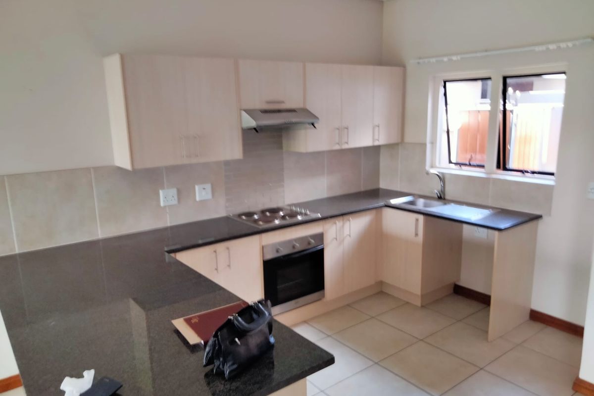 A functional kitchen featuring light wood cabinetry, dark granite countertops, built-in oven and hob, and tiled flooring.