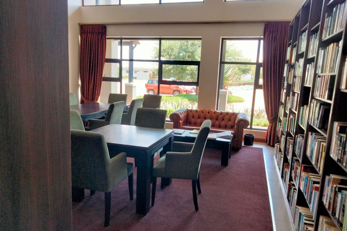 A communal library and lounge area featuring extensive built-in bookshelves, large windows providing natural light, and comfortable seating arrangements.