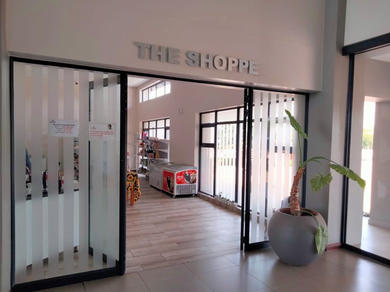 Entrance to the village shop featuring modern tiled flooring and large glass sliding doors, providing a welcoming and accessible retail space for residents.