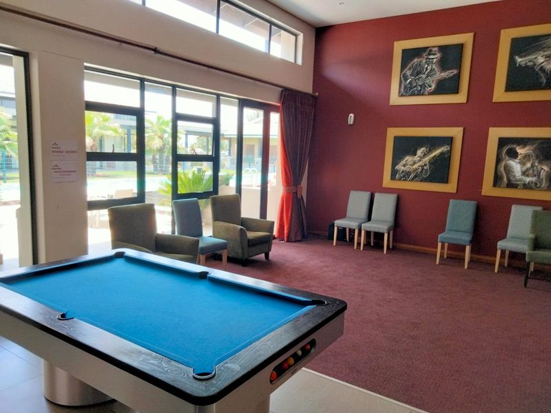 A spacious clubhouse lounge area featuring high ceilings, large windows providing natural light, and carpeted flooring, suitable for social gatherings and recreation.