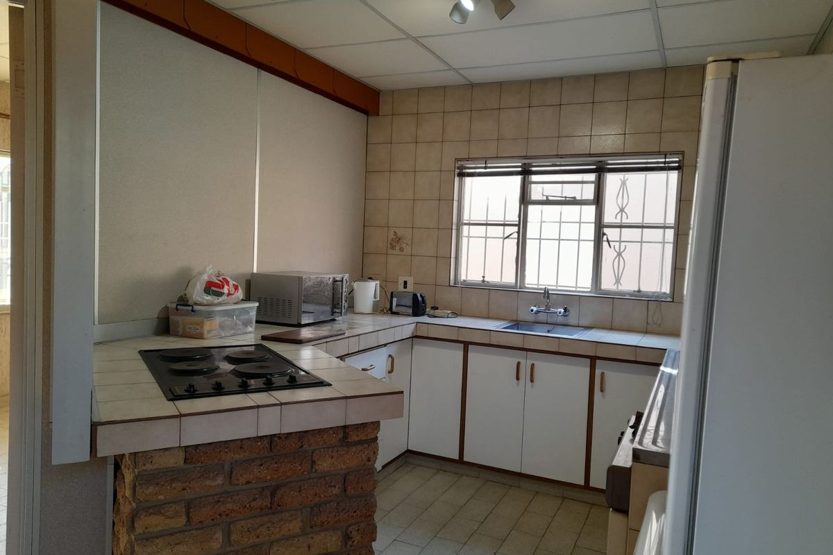 A dated kitchen featuring brick-based cabinetry, tiled countertops, a built-in electric hob, and a stainless steel sink with security-barred windows.
