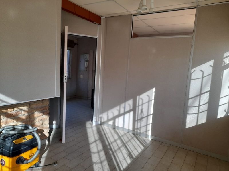 An empty living area featuring tiled flooring, a brick fireplace, and a suspended ceiling, with an adjacent room visible through an open doorway.
