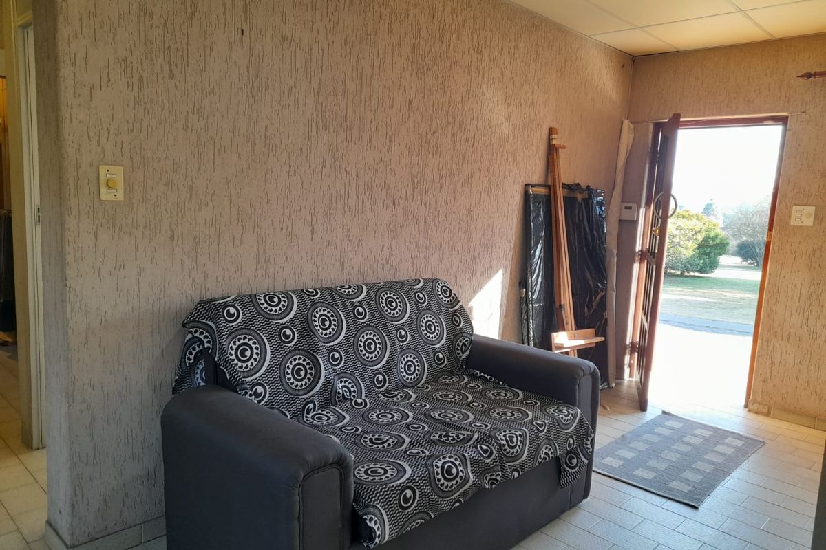 A living area featuring textured walls, tiled flooring, and a drop ceiling, with direct access to the exterior garden.