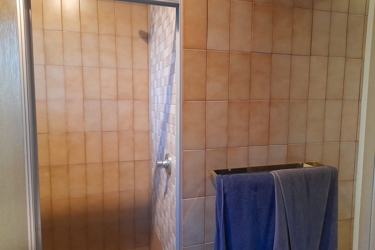 A functional bathroom shower area featuring dated ceramic wall tiling and a built-in shower enclosure with a metal frame.