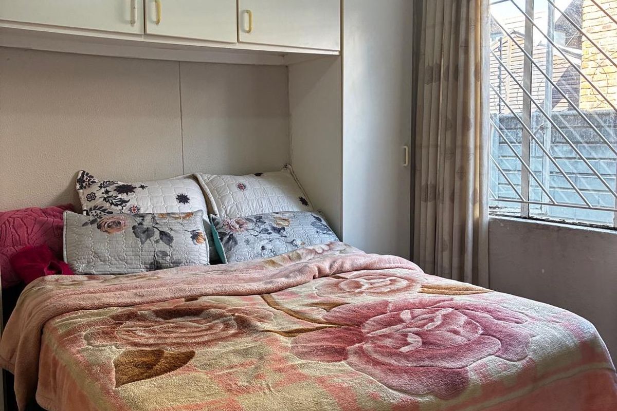 A bedroom featuring built-in overhead cupboards, tiled flooring, and security bars on the window.