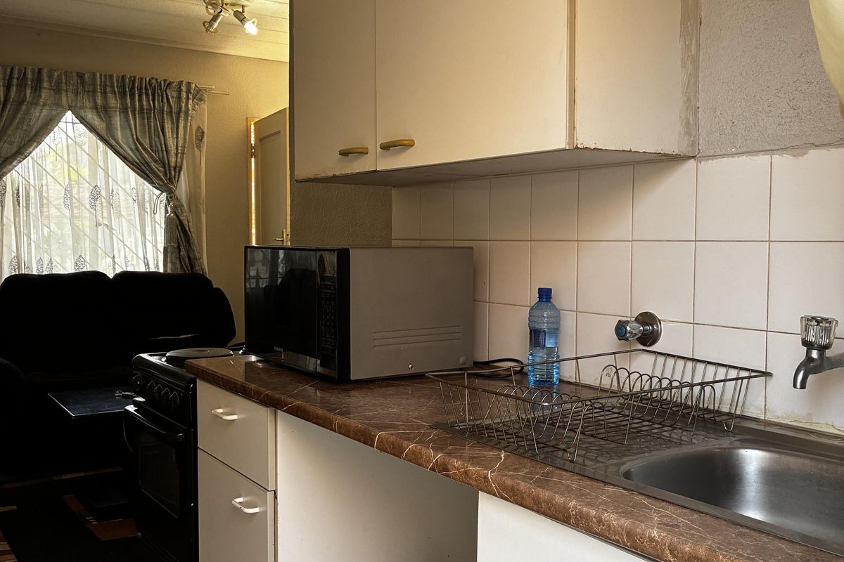 A compact kitchen featuring laminate countertops, a stainless steel sink, and wall-mounted cabinetry, showing signs of age and requiring cosmetic updates.