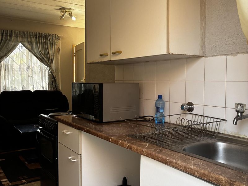 A compact kitchen featuring laminate countertops, a stainless steel sink, and wall-mounted cabinetry, showing signs of age and requiring cosmetic updates.