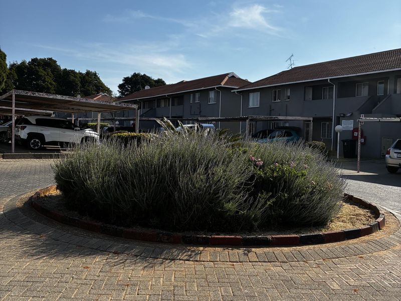 Exterior view of the apartment complex featuring a paved driveway, covered parking bays, and a central landscaped garden bed.