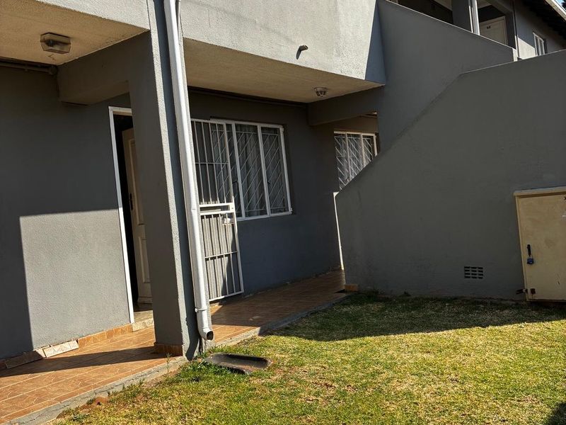 Rear exterior view of the apartment building featuring a small tiled patio area, security gates, and a private lawn space.
