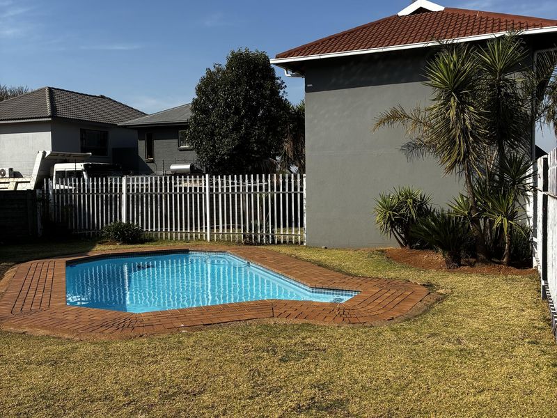 Outdoor pool area featuring a swimming pool with brick coping, set within a private garden with perimeter fencing and a tiled roof structure.