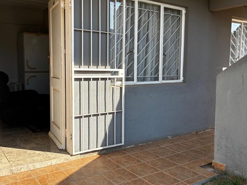 A rear exterior view of the apartment featuring a tiled patio area, security gate, and window security bars.