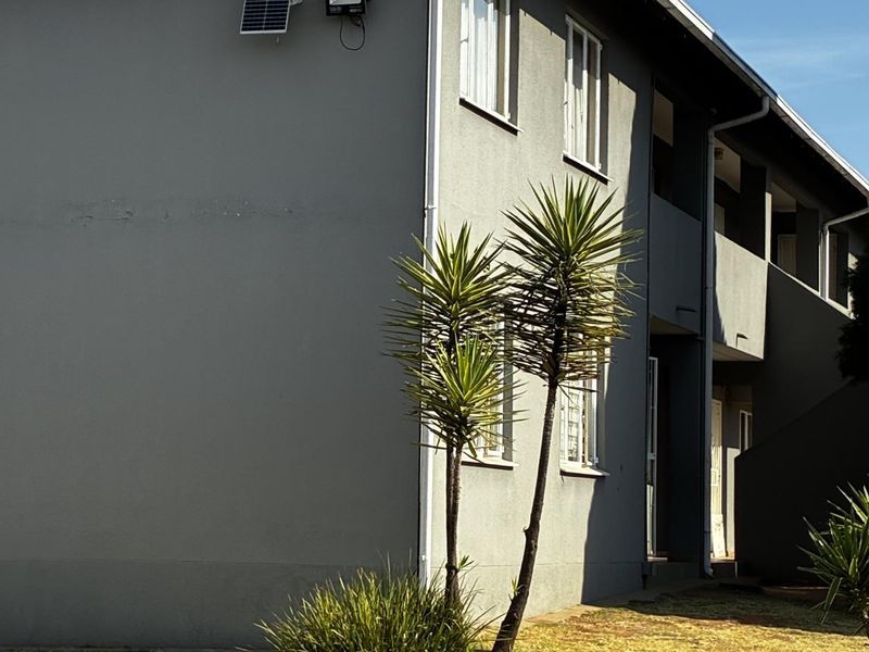 A view of the apartment building exterior featuring a grey facade, tiled roof, and solar-powered security lighting with a small landscaped garden area.