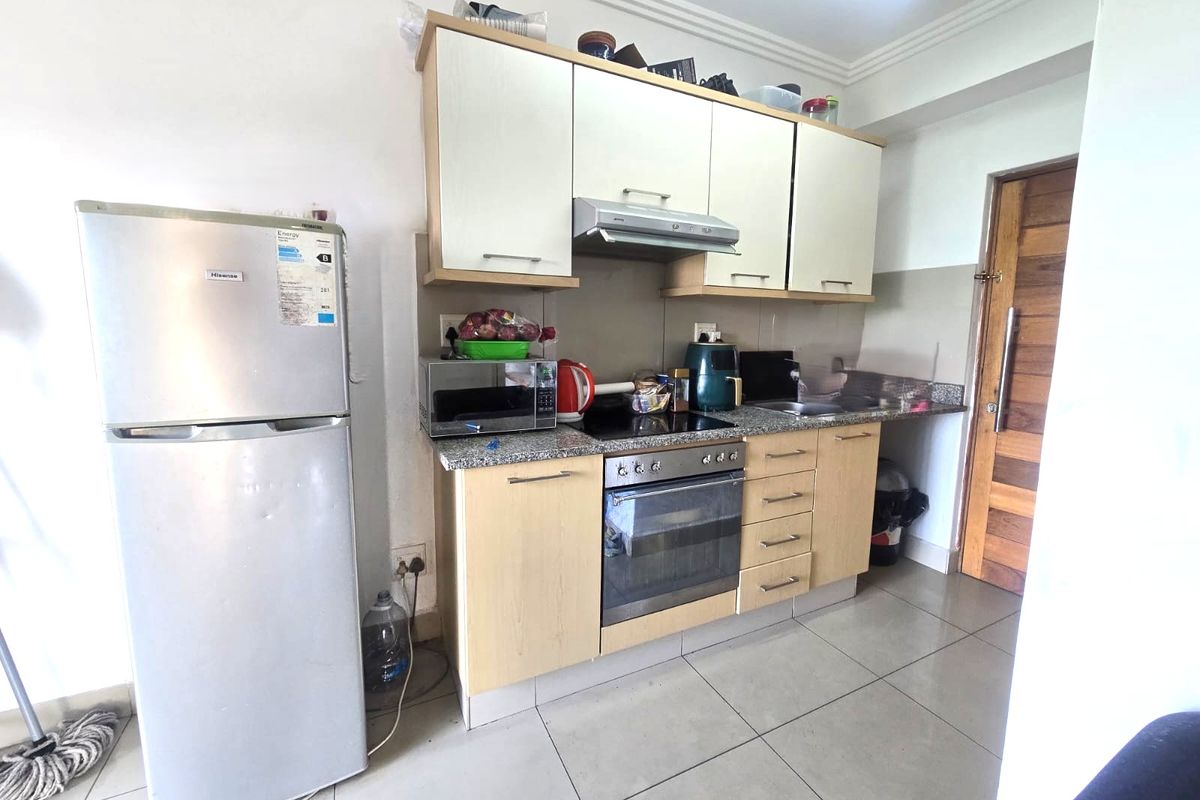 Compact kitchen featuring light wood-finish cabinetry, granite countertops, built-in oven with hob, extractor fan, and tiled flooring.