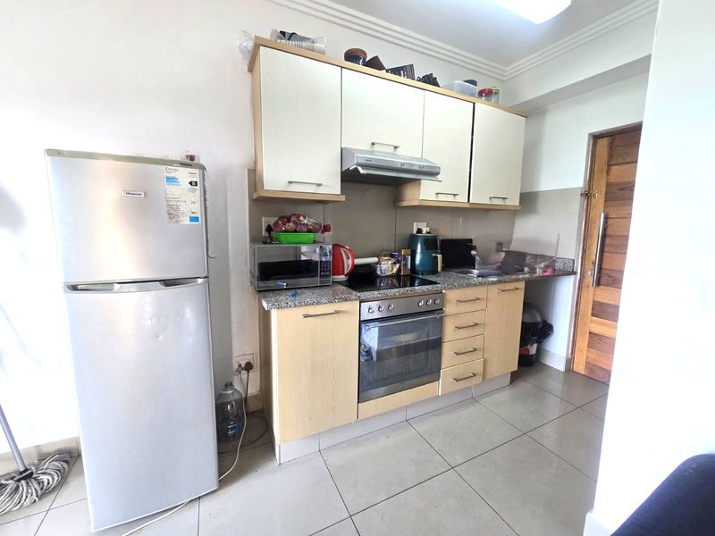 Compact kitchen featuring light wood-finish cabinetry, granite countertops, built-in oven with hob, extractor fan, and tiled flooring.