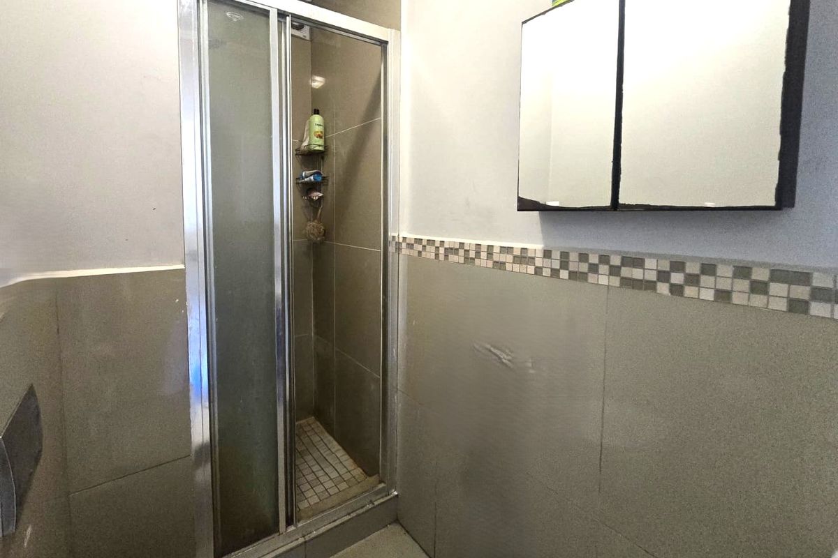 A functional bathroom featuring a shower enclosure with tiled walls, a mosaic border, and a wall-mounted medicine cabinet.