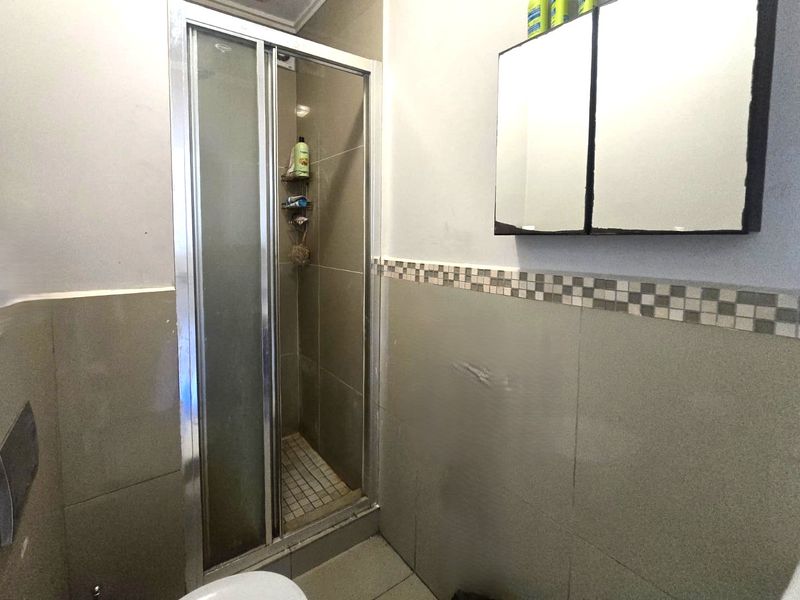 A functional bathroom featuring a shower enclosure with tiled walls, a mosaic border, and a wall-mounted medicine cabinet.