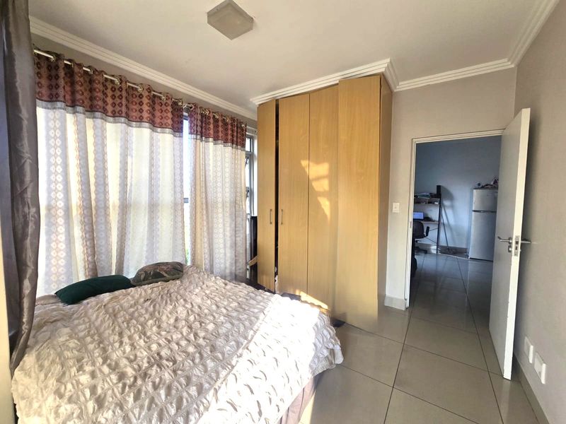 A bedroom featuring tiled flooring, a built-in wooden wardrobe, and ceiling cornice detailing, with an adjacent view into a secondary living space.