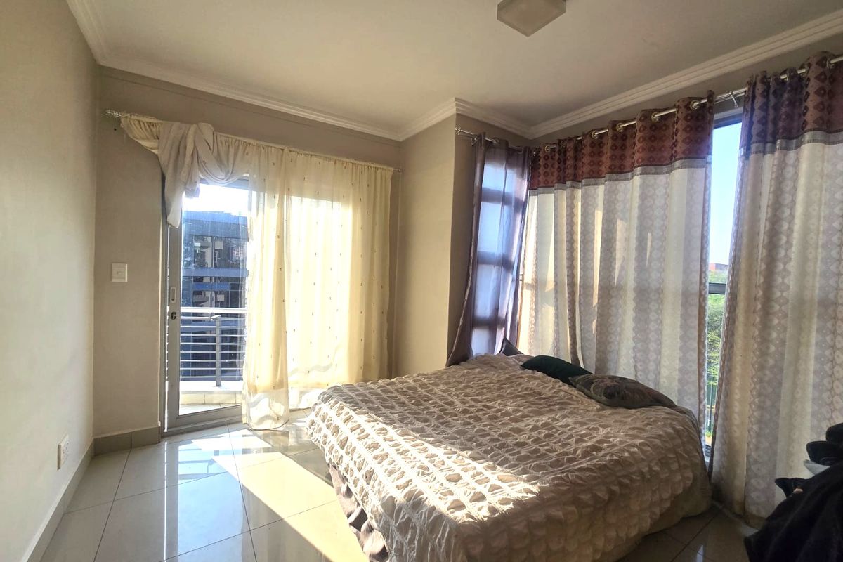 A bright bedroom featuring tiled flooring, large windows, and a sliding glass door providing access to a balcony.