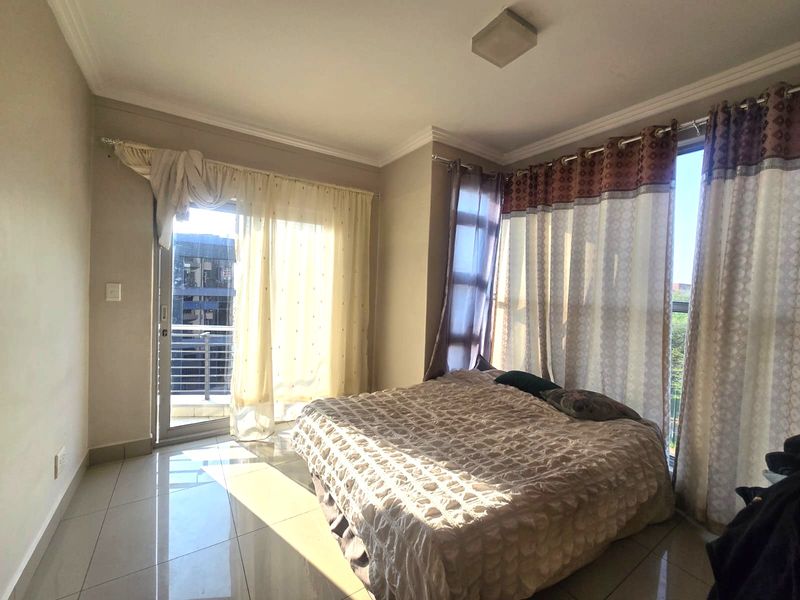 A bright bedroom featuring tiled flooring, large windows, and a sliding glass door providing access to a balcony.