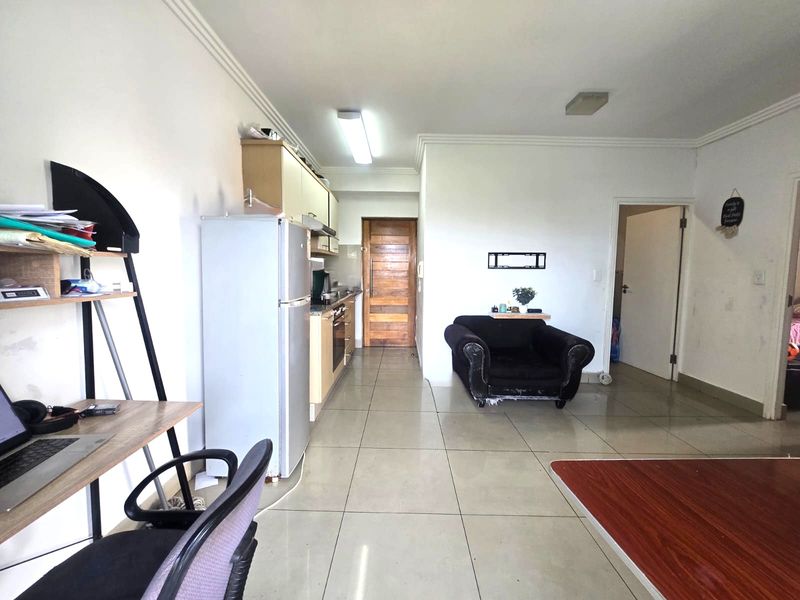 Open-plan living area featuring tiled flooring, a functional kitchen with built-in cabinetry and appliances, and access to adjacent rooms.