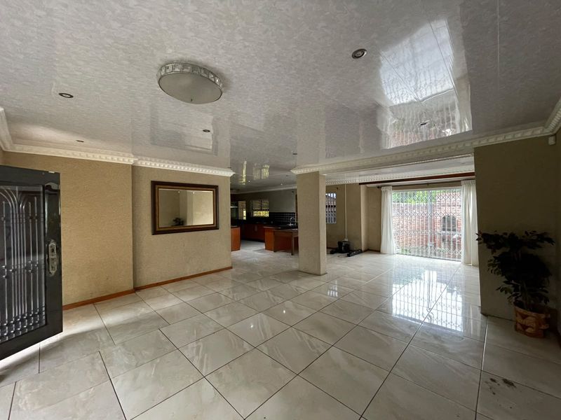 Spacious open-plan living area featuring high-gloss ceilings, recessed lighting, and large porcelain floor tiles, leading to a bright rear patio area.