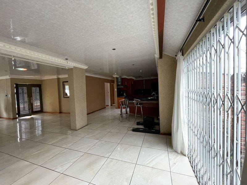 Spacious open-plan living and kitchen area featuring large format floor tiles, decorative ceiling cornices, and a secure entrance with integrated security gates.