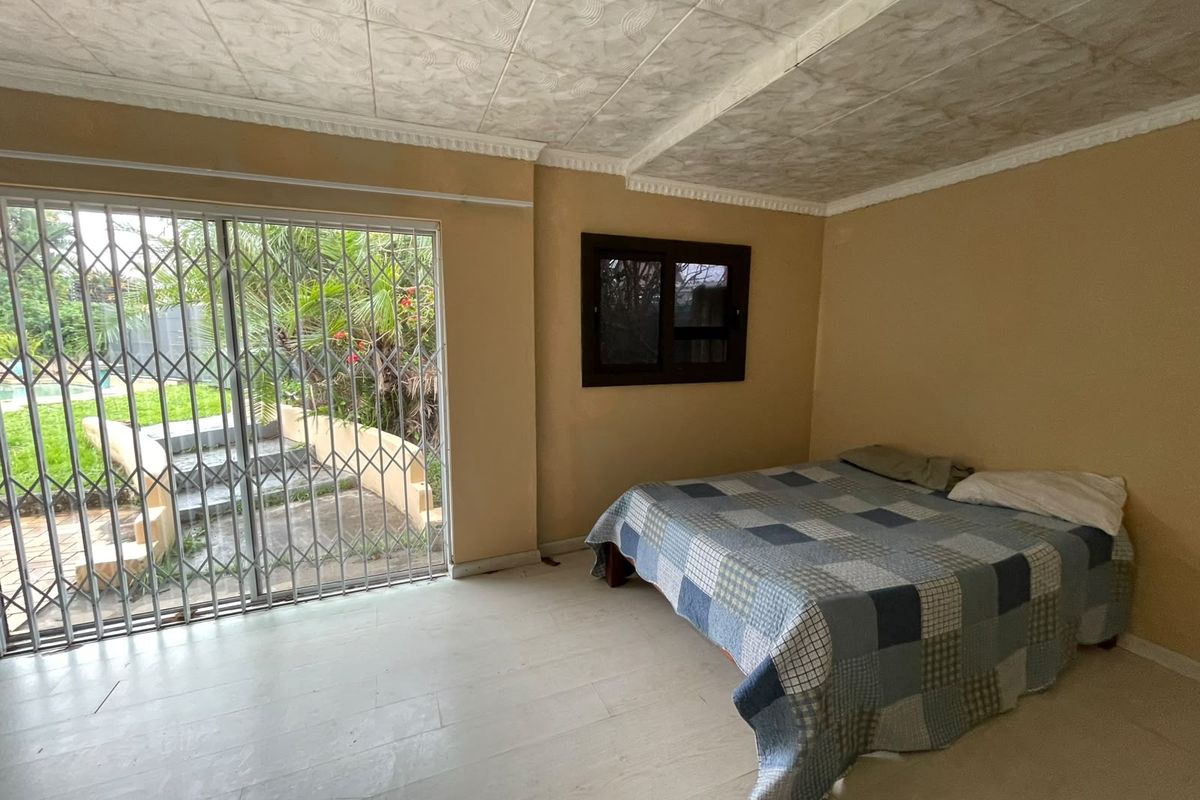 A bedroom featuring tiled flooring, a textured ceiling, and a sliding glass door with a security gate providing access to the garden.