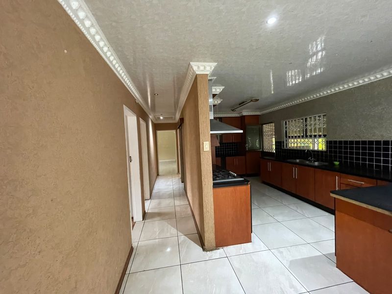 Spacious kitchen featuring built-in wooden cabinetry, gas hob, extractor fan, and tiled flooring, offering a functional layout with ample storage space.