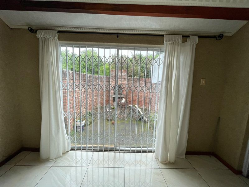 Living area featuring tiled floors and a sliding glass door with security gate, opening onto a private courtyard with a built-in brick braai.