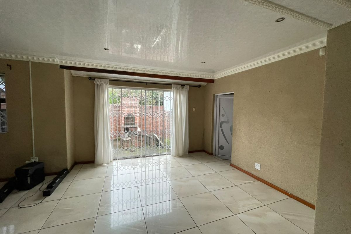 An empty living room featuring tiled flooring, decorative ceiling cornices, and a security gate leading to an outdoor area.