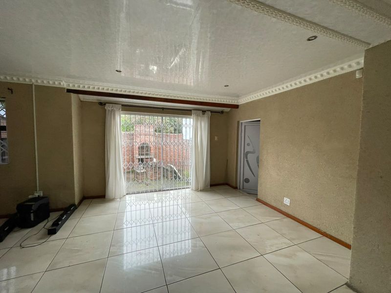 An empty living room featuring tiled flooring, decorative ceiling cornices, and a security gate leading to an outdoor area.