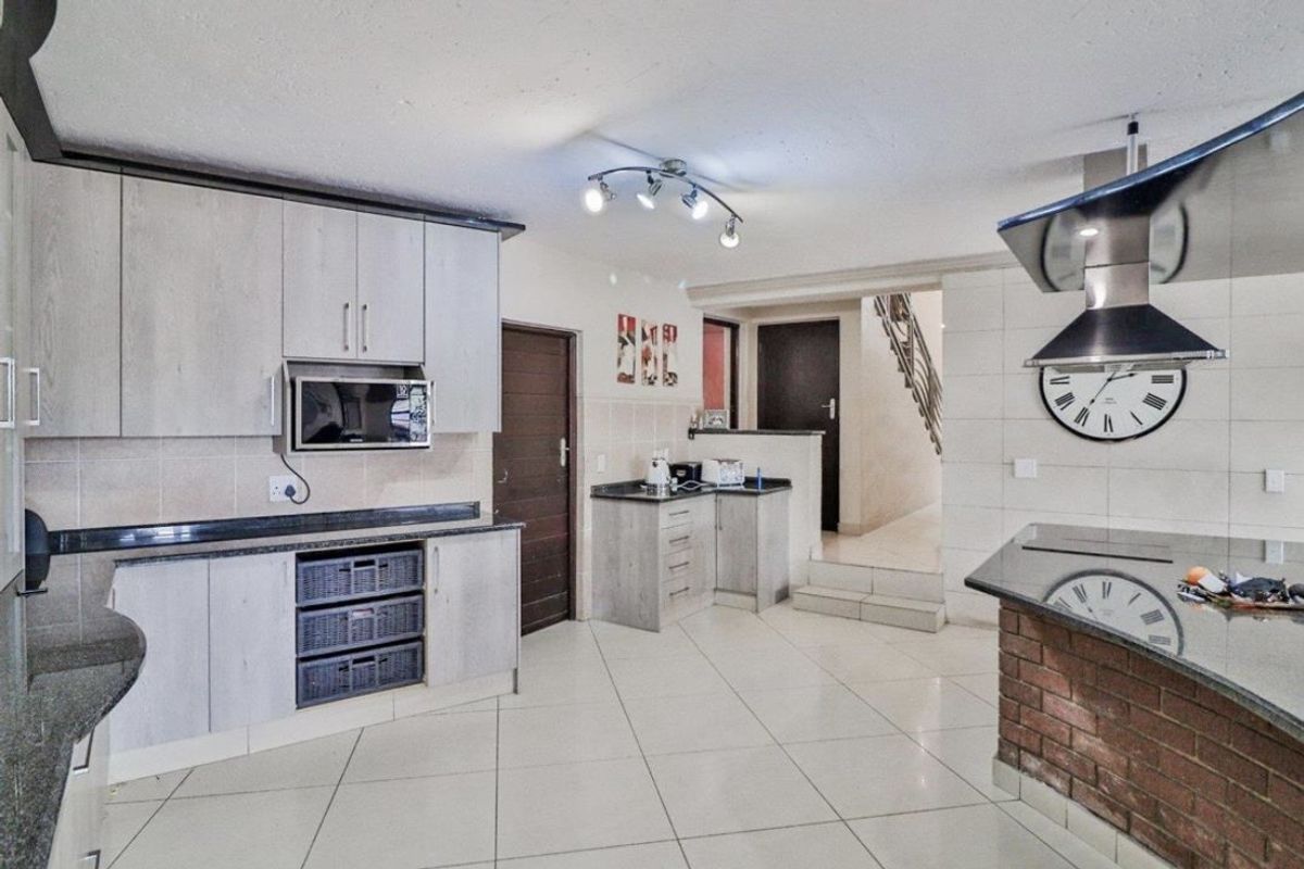 Modern kitchen featuring light wood cabinetry, granite countertops, tiled flooring, and an integrated extractor fan, with an open-plan layout leading to a staircase.