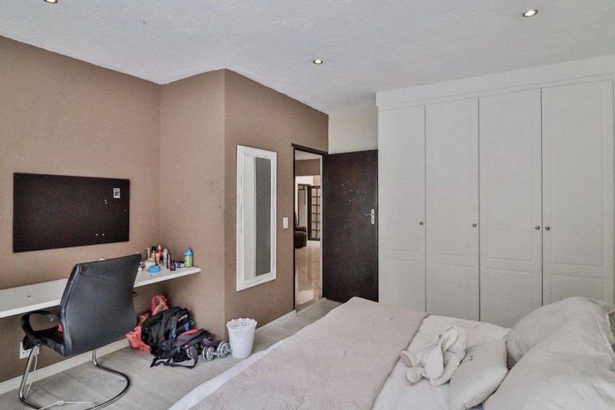 A bedroom featuring built-in cupboards, recessed downlighting, and a wall-mounted floating desk, providing a functional space with neutral wall finishes.