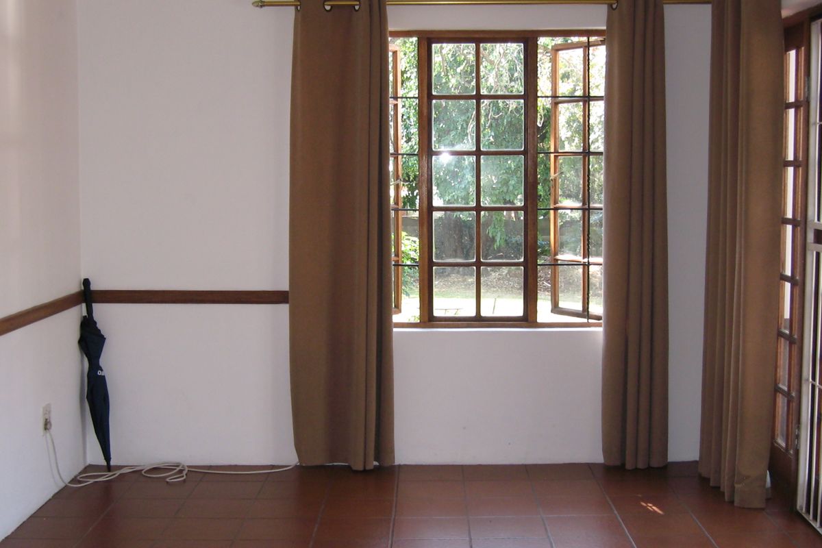 An empty living room featuring terracotta floor tiles, timber-framed windows, and a timber dado rail, offering a bright and neutral space.