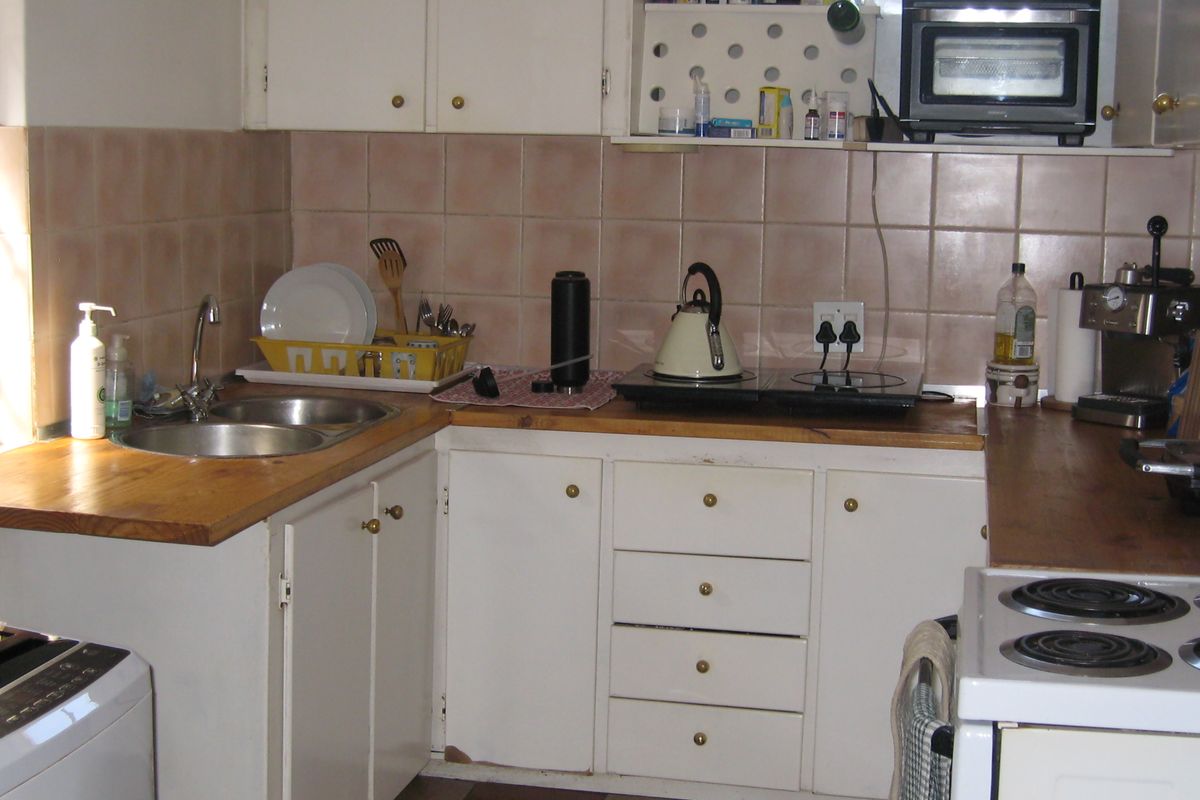 A compact kitchen featuring wooden countertops, white built-in cabinetry, a double bowl sink, and tiled backsplash with ceramic floor tiles.