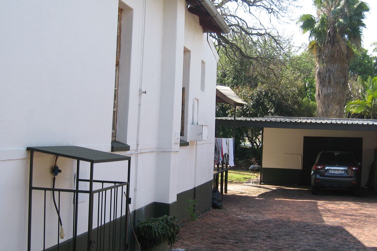 Rear exterior view showing a paved driveway, a carport structure, and the side elevation of the house with a gas cylinder storage cage.