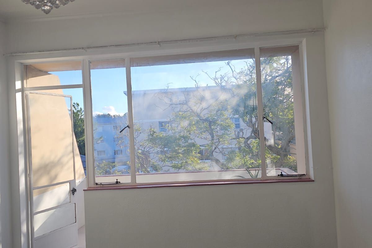 An empty living room featuring large windows, carpeted flooring, and access to an outdoor balcony area.